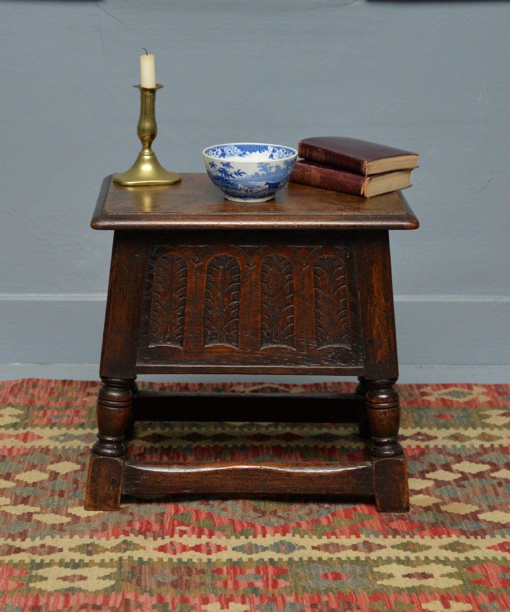 A dark oak box stool featuring carved arched panels, turned baluster legs, and a rectangular top. View V