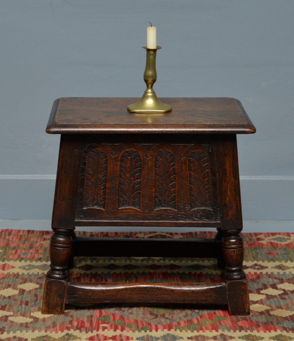 A dark oak box stool featuring carved arched panels, turned baluster legs, and a rectangular top. View VI