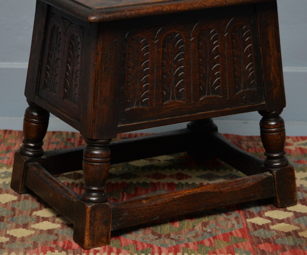 A dark oak box stool featuring carved arched panels, turned baluster legs, and a rectangular top. View VII