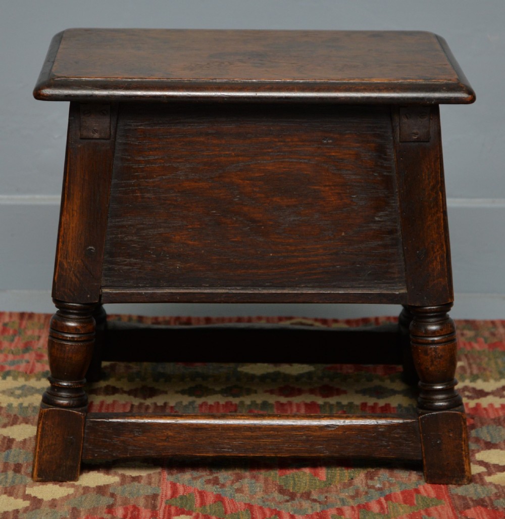 A dark oak box stool featuring carved arched panels, turned baluster legs, and a rectangular top. View XI