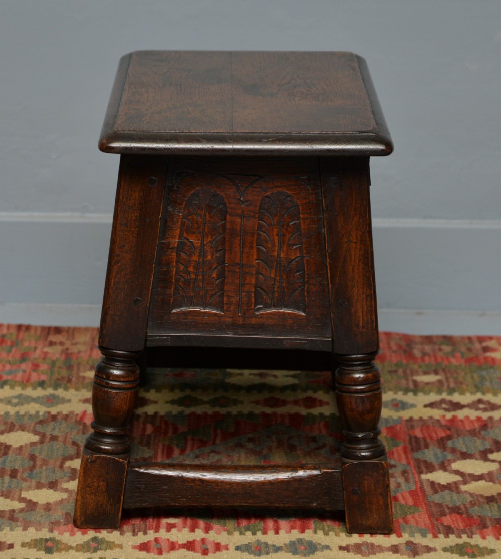 A dark oak box stool featuring carved arched panels, turned baluster legs, and a rectangular top. View XII