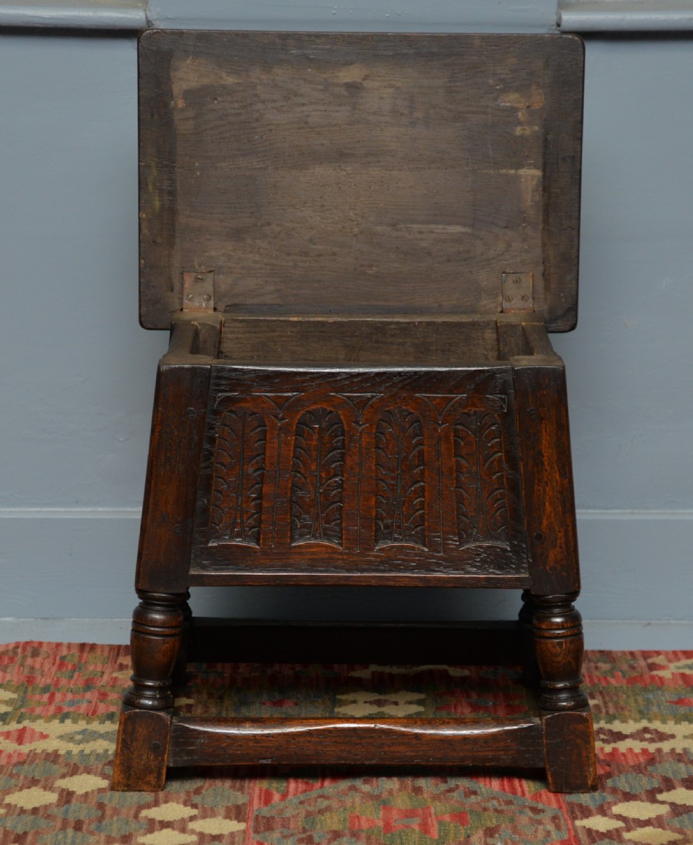 A dark oak box stool featuring carved arched panels, turned baluster legs, and a rectangular top. View XIII