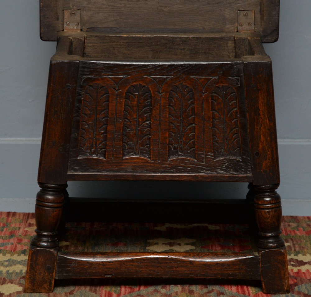 A dark oak box stool featuring carved arched panels, turned baluster legs, and a rectangular top. View XIV