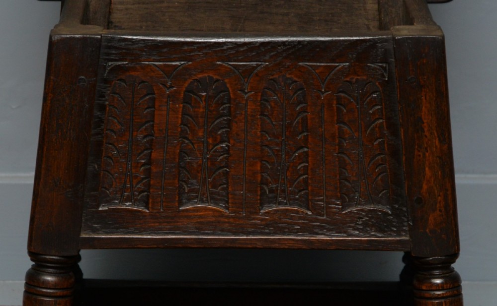 A dark oak box stool featuring carved arched panels, turned baluster legs, and a rectangular top. View XV