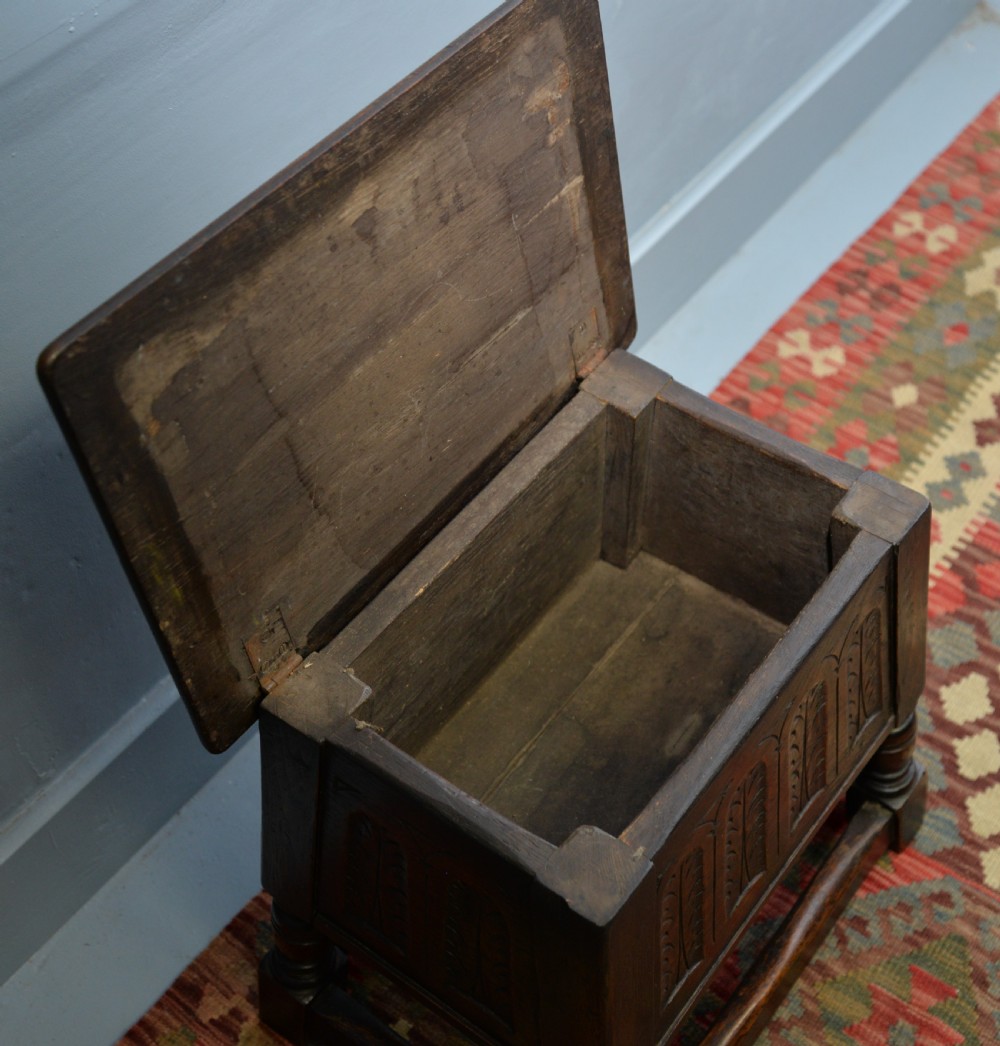 A dark oak box stool featuring carved arched panels, turned baluster legs, and a rectangular top. View XVI