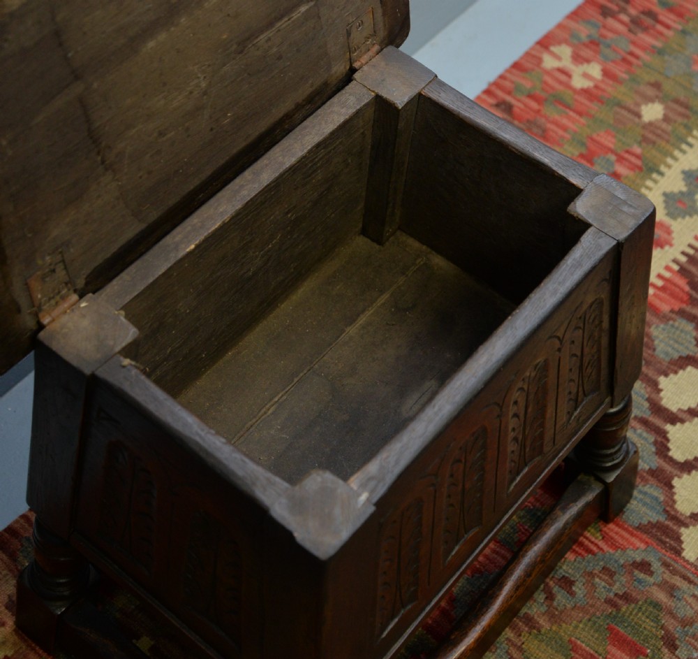 A dark oak box stool featuring carved arched panels, turned baluster legs, and a rectangular top. View XVII