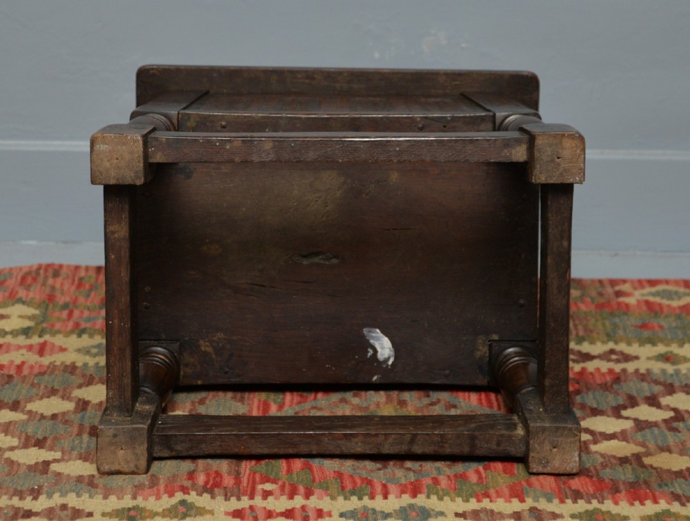 A dark oak box stool featuring carved arched panels, turned baluster legs, and a rectangular top. View XX