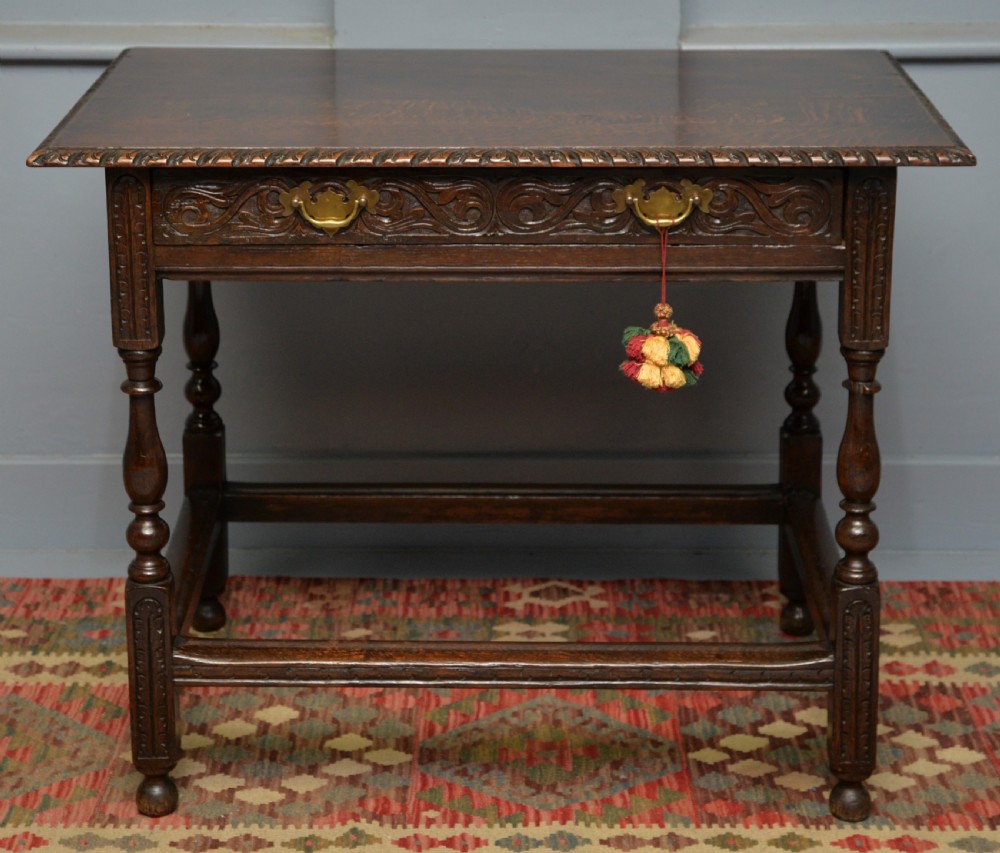 A dark carved oak side table featuring a single scroll-carved frieze drawer, turned legs, and a lower stretcher frame.