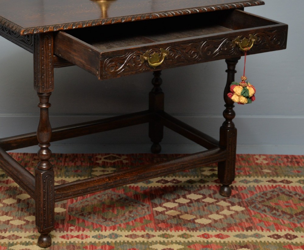 A dark carved oak side table featuring a single scroll-carved frieze drawer, turned legs, and a lower stretcher frame. View X