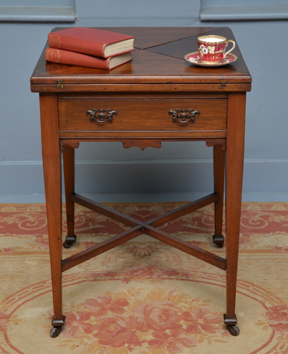 An antique mahogany envelope card table featuring four triangular top flaps, a single drawer with brass drop handles, and tapered legs joined by an X-shaped stretcher. View II