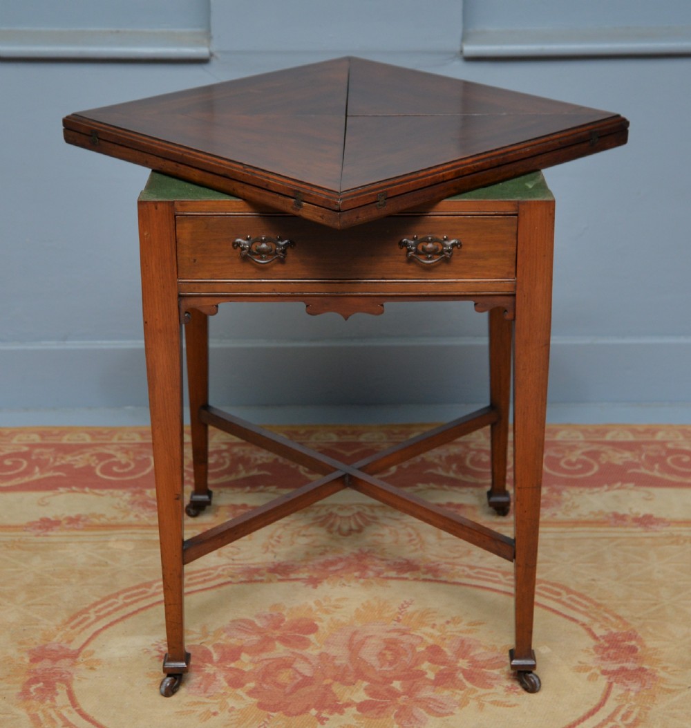 An antique mahogany envelope card table featuring four triangular top flaps, a single drawer with brass drop handles, and tapered legs joined by an X-shaped stretcher. View VI