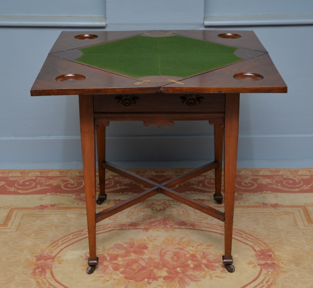 An antique mahogany envelope card table featuring four triangular top flaps, a single drawer with brass drop handles, and tapered legs joined by an X-shaped stretcher. View VII