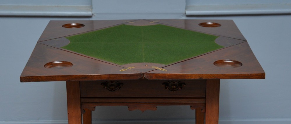 An antique mahogany envelope card table featuring four triangular top flaps, a single drawer with brass drop handles, and tapered legs joined by an X-shaped stretcher. View VIII
