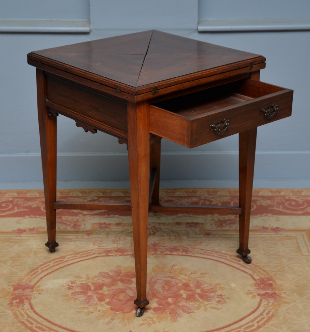 An antique mahogany envelope card table featuring four triangular top flaps, a single drawer with brass drop handles, and tapered legs joined by an X-shaped stretcher. View IX