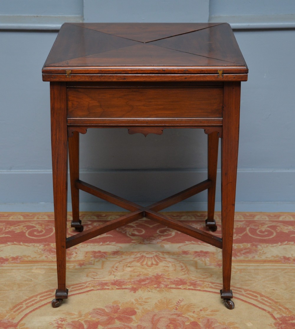 An antique mahogany envelope card table featuring four triangular top flaps, a single drawer with brass drop handles, and tapered legs joined by an X-shaped stretcher. View XII