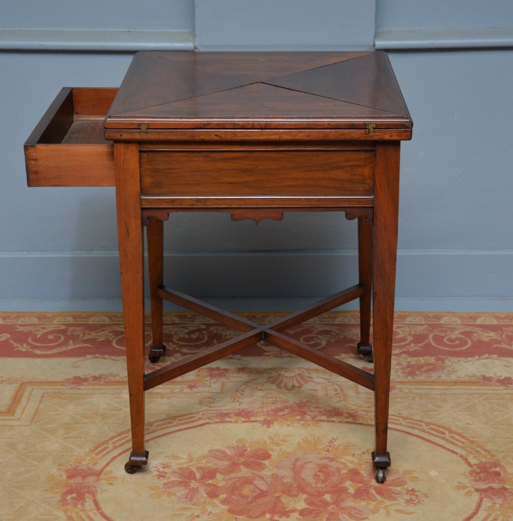 An antique mahogany envelope card table featuring four triangular top flaps, a single drawer with brass drop handles, and tapered legs joined by an X-shaped stretcher. View XIII