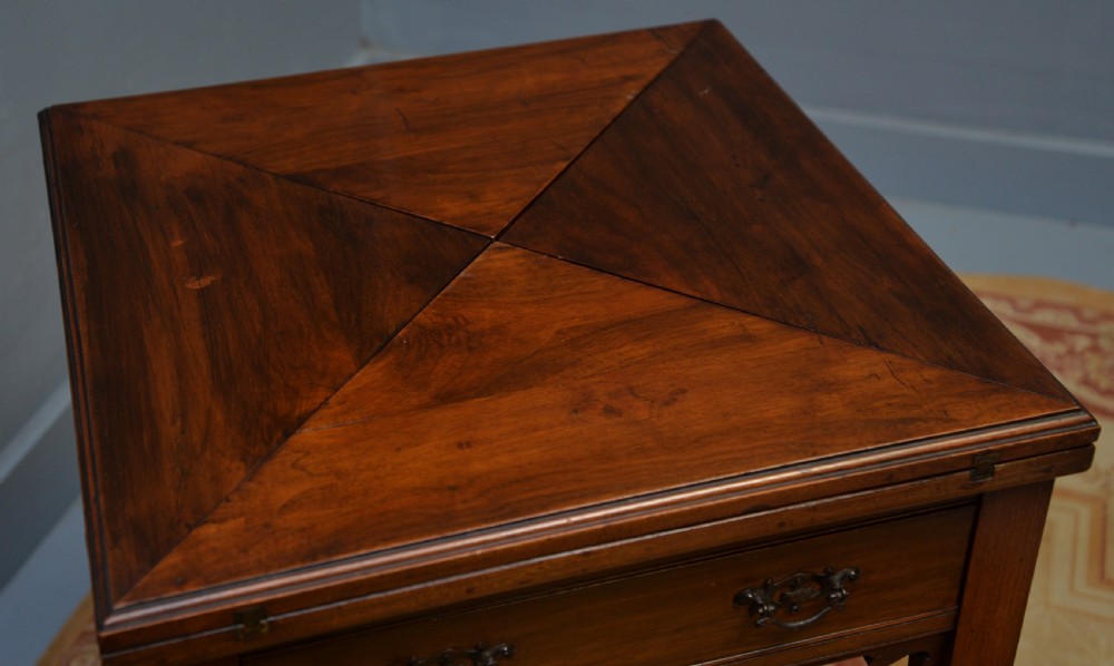 An antique mahogany envelope card table featuring four triangular top flaps, a single drawer with brass drop handles, and tapered legs joined by an X-shaped stretcher. View XV