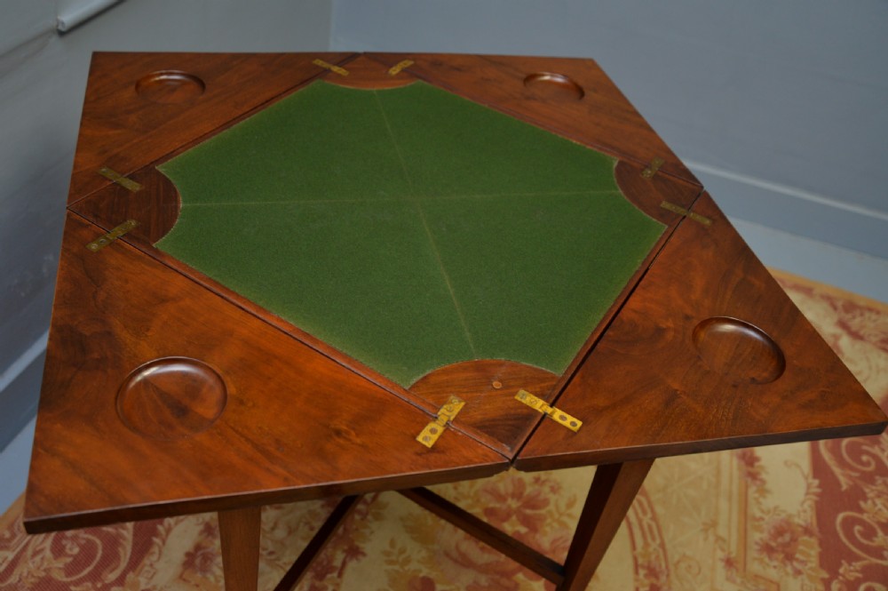 An antique mahogany envelope card table featuring four triangular top flaps, a single drawer with brass drop handles, and tapered legs joined by an X-shaped stretcher. View XVI