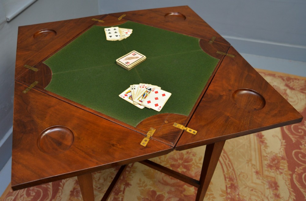 An antique mahogany envelope card table featuring four triangular top flaps, a single drawer with brass drop handles, and tapered legs joined by an X-shaped stretcher. View XVII