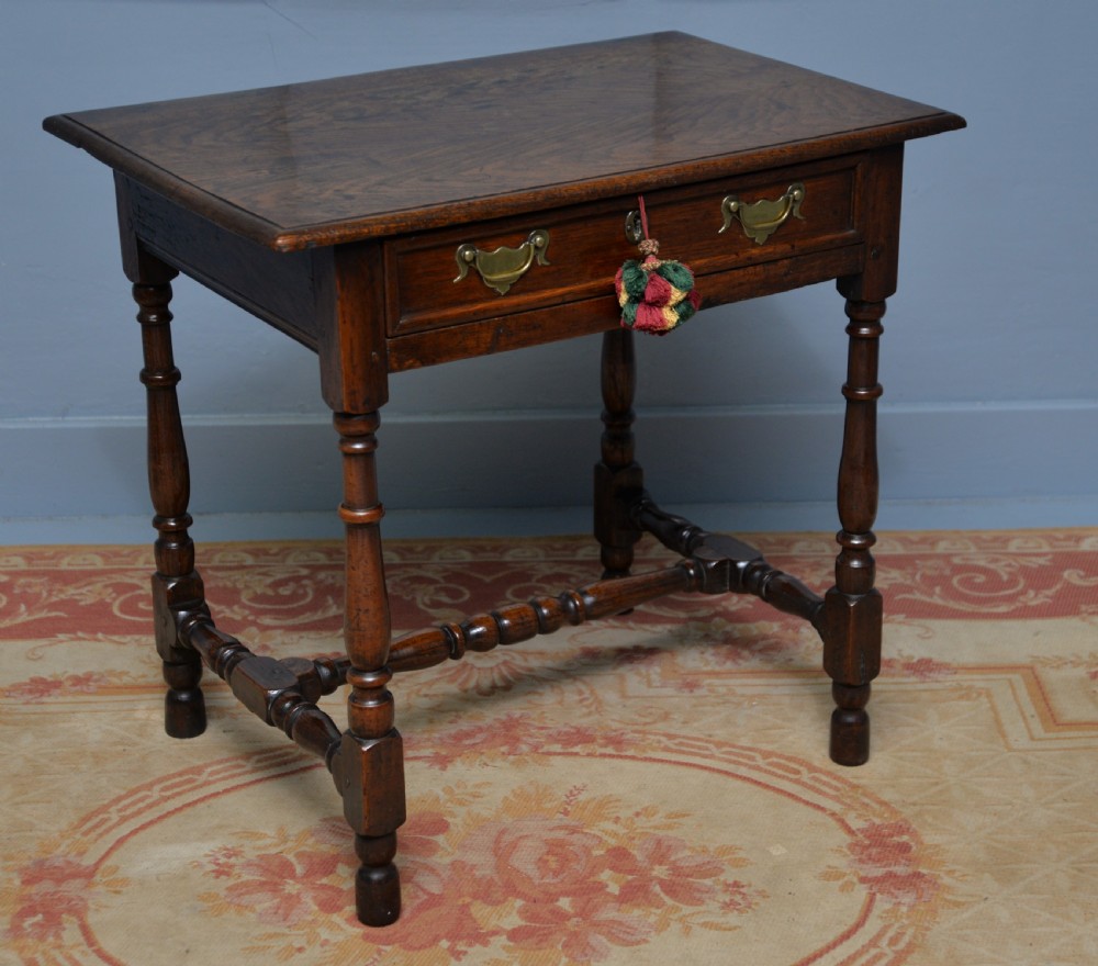 An early 18th-century dark oak side table featuring a rectangular top, single frieze drawer with brass handles, turned legs, and a stretcher base.
