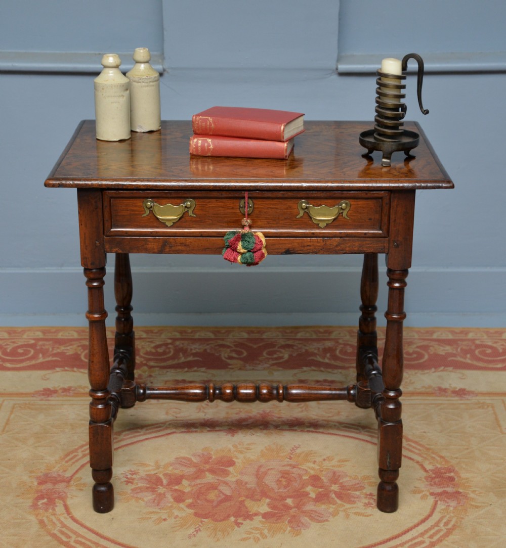 An early 18th-century dark oak side table featuring a rectangular top, single frieze drawer with brass handles, turned legs, and a stretcher base. View II