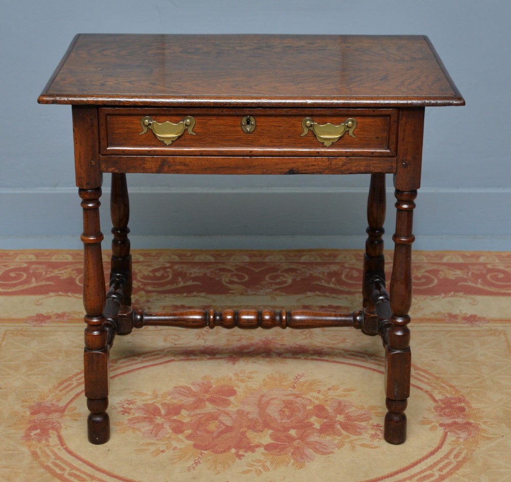 An early 18th-century dark oak side table featuring a rectangular top, single frieze drawer with brass handles, turned legs, and a stretcher base. View V