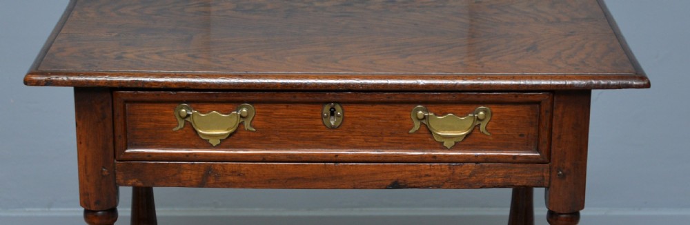 An early 18th-century dark oak side table featuring a rectangular top, single frieze drawer with brass handles, turned legs, and a stretcher base. View VI