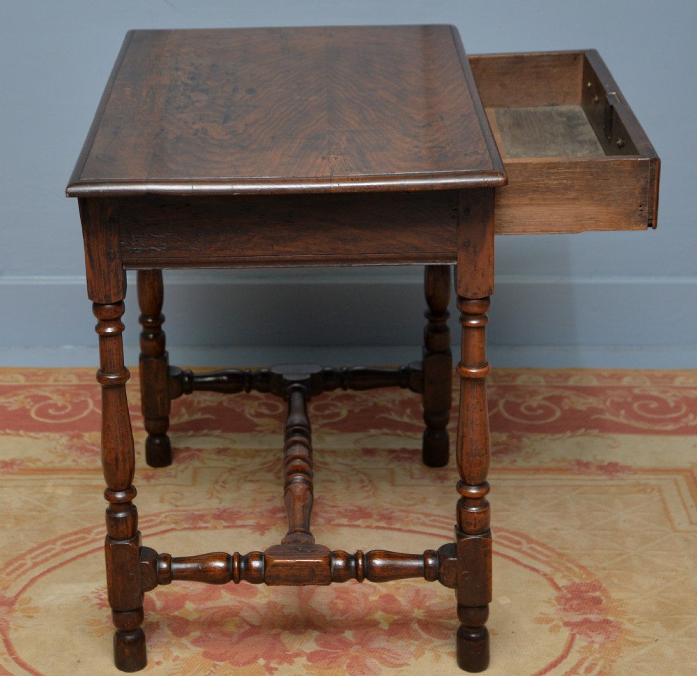 An early 18th-century dark oak side table featuring a rectangular top, single frieze drawer with brass handles, turned legs, and a stretcher base. View VII