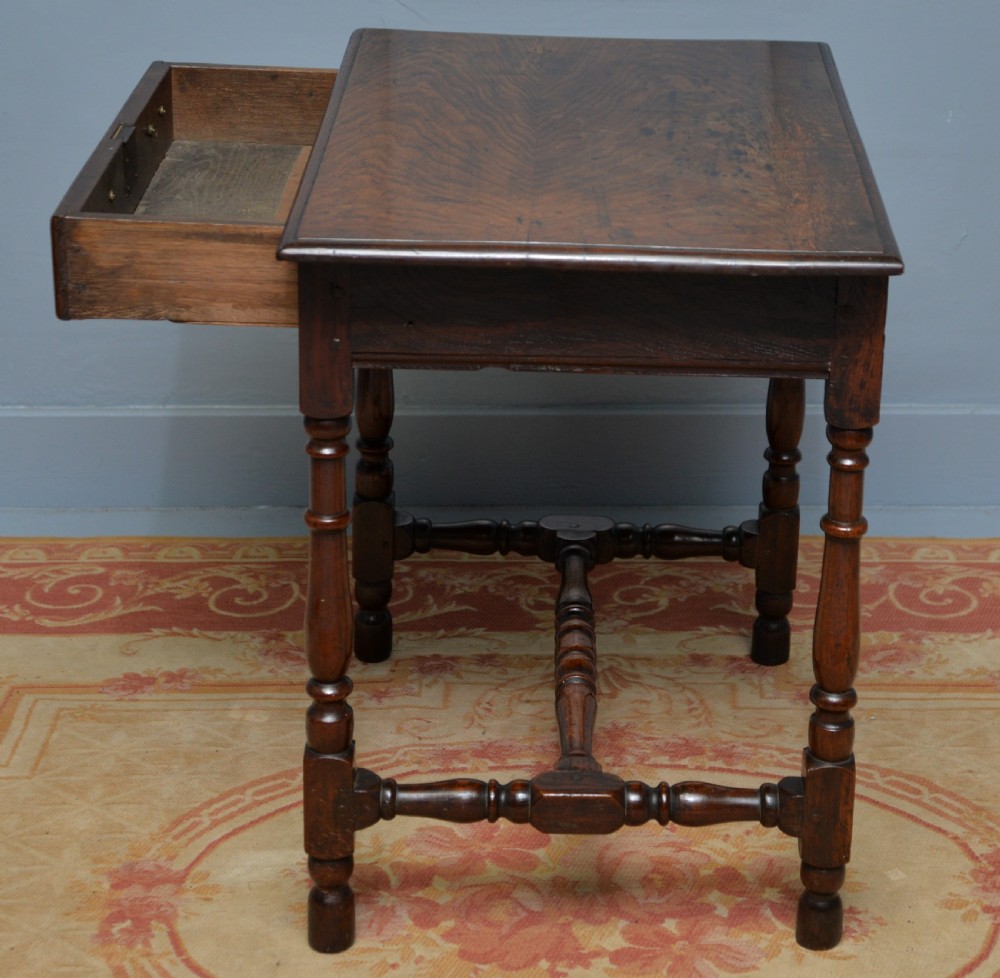 An early 18th-century dark oak side table featuring a rectangular top, single frieze drawer with brass handles, turned legs, and a stretcher base. View IX
