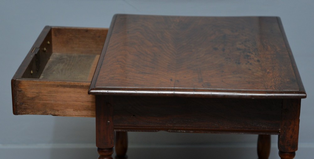 An early 18th-century dark oak side table featuring a rectangular top, single frieze drawer with brass handles, turned legs, and a stretcher base. View X