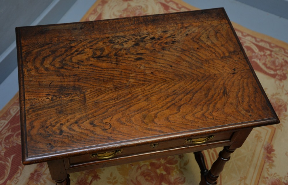 An early 18th-century dark oak side table featuring a rectangular top, single frieze drawer with brass handles, turned legs, and a stretcher base. View XI
