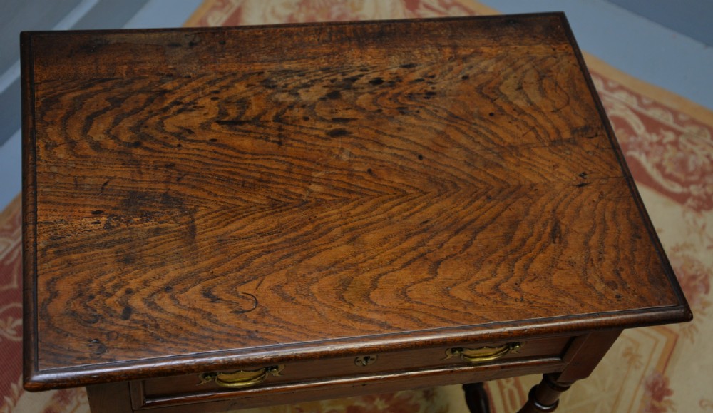 An early 18th-century dark oak side table featuring a rectangular top, single frieze drawer with brass handles, turned legs, and a stretcher base. View XII