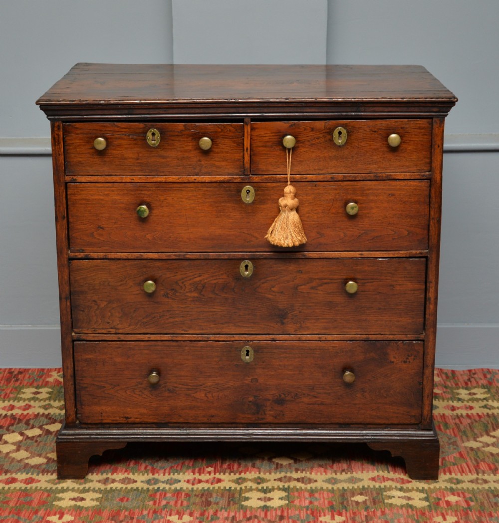 An early eighteenth-century Georgian oak chest of drawers featuring a two-over-three drawer configuration, brass escutcheons, turned knobs, and shaped bracket feet.