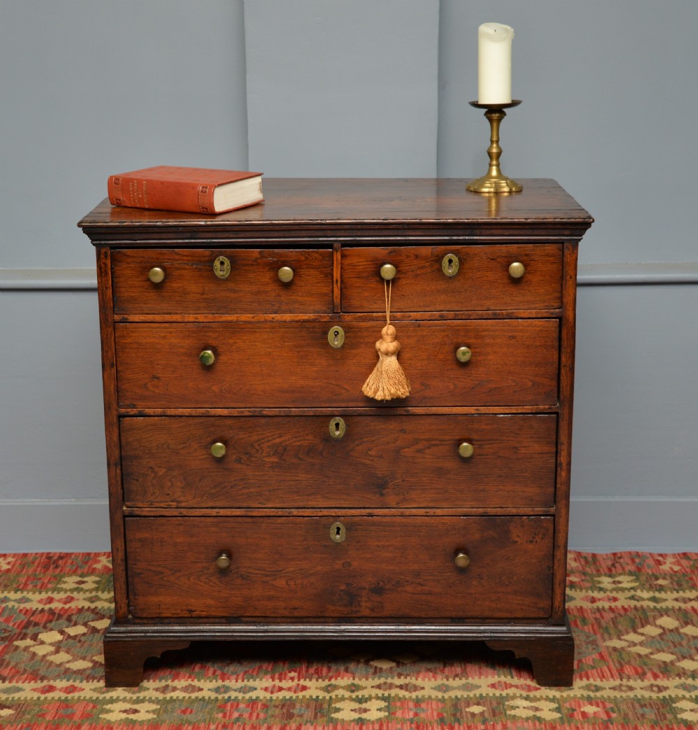 An early eighteenth-century Georgian oak chest of drawers featuring a two-over-three drawer configuration, brass escutcheons, turned knobs, and shaped bracket feet. View II