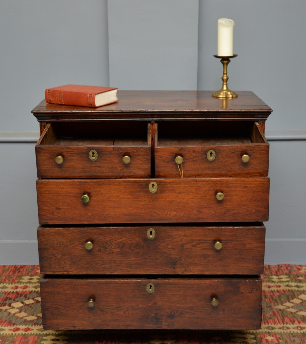 An early eighteenth-century Georgian oak chest of drawers featuring a two-over-three drawer configuration, brass escutcheons, turned knobs, and shaped bracket feet. View III