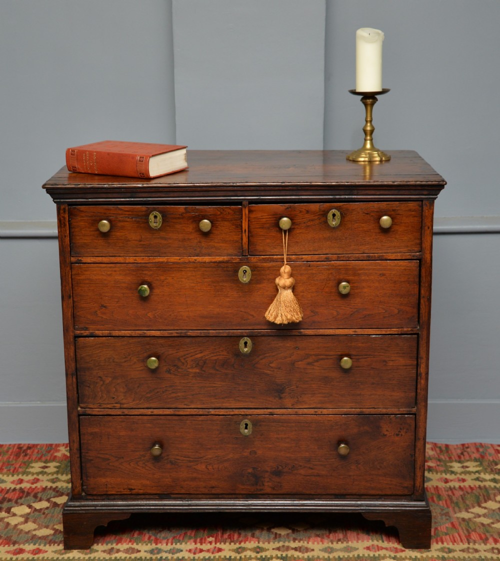 An early eighteenth-century Georgian oak chest of drawers featuring a two-over-three drawer configuration, brass escutcheons, turned knobs, and shaped bracket feet. View IV