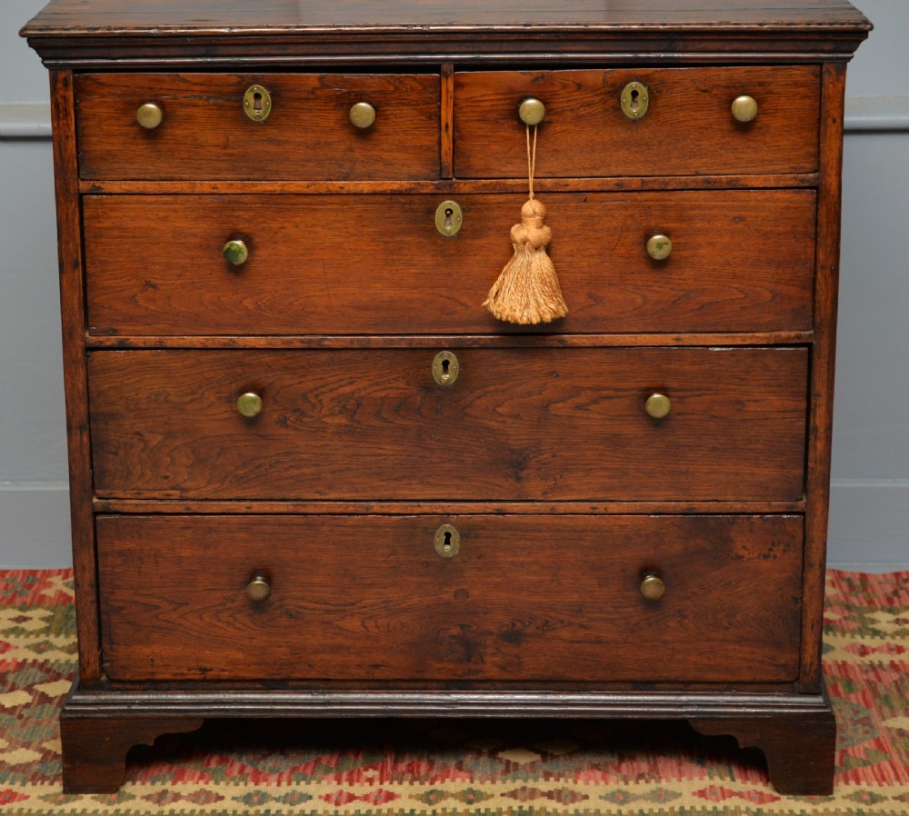 An early eighteenth-century Georgian oak chest of drawers featuring a two-over-three drawer configuration, brass escutcheons, turned knobs, and shaped bracket feet. View VI