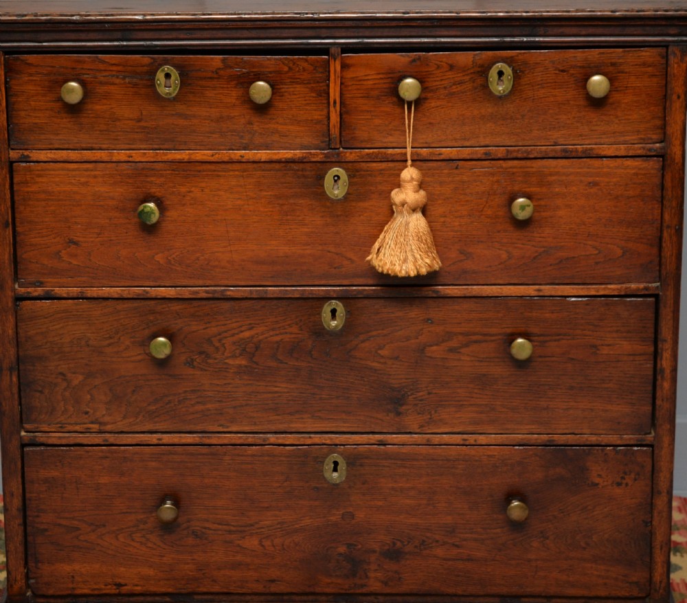 An early eighteenth-century Georgian oak chest of drawers featuring a two-over-three drawer configuration, brass escutcheons, turned knobs, and shaped bracket feet. View VII