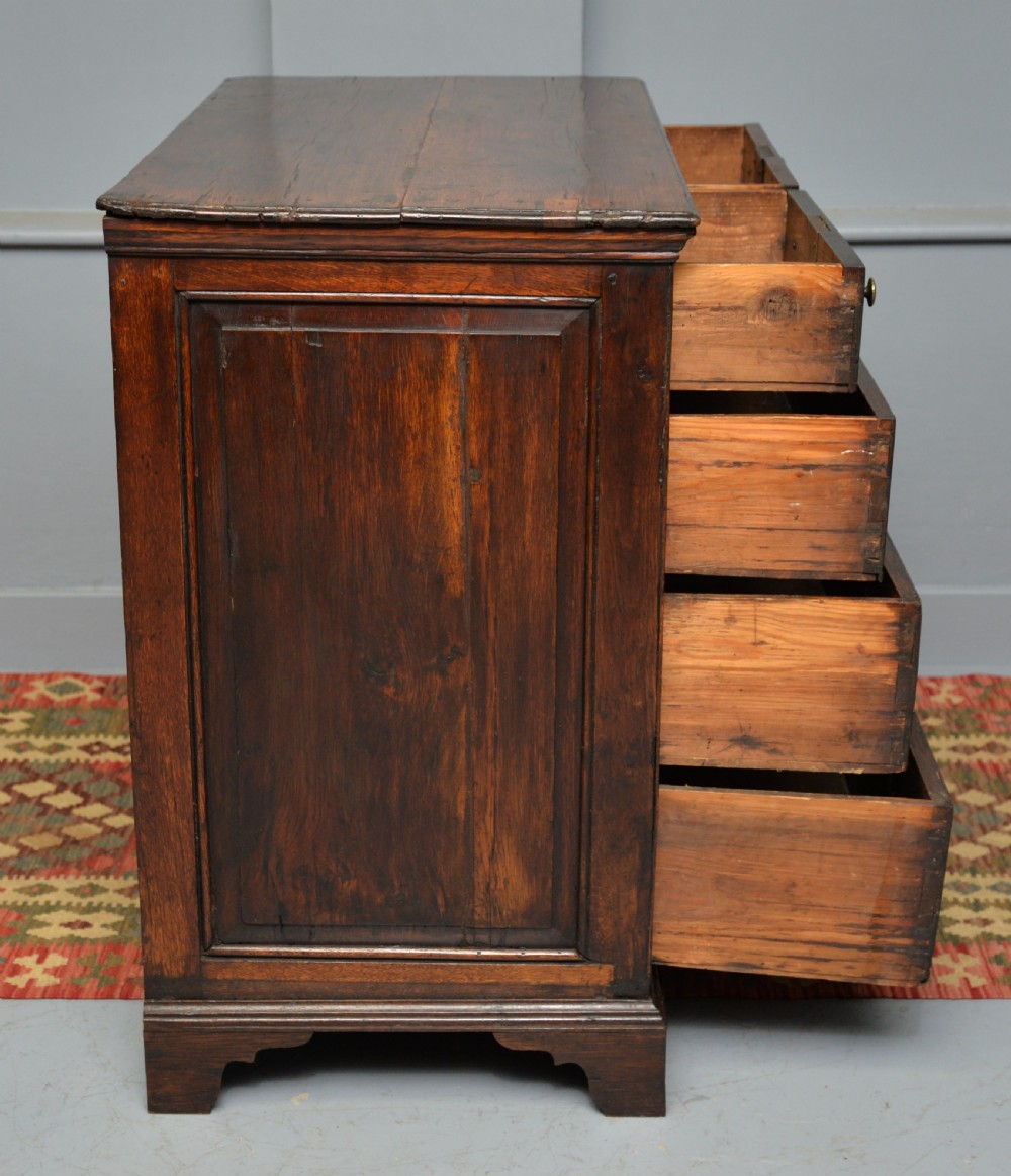 An early eighteenth-century Georgian oak chest of drawers featuring a two-over-three drawer configuration, brass escutcheons, turned knobs, and shaped bracket feet. View VIII