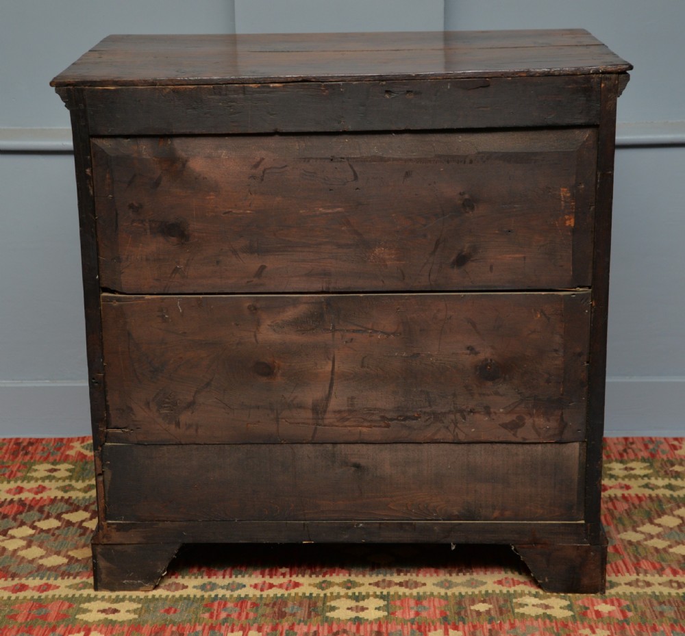 An early eighteenth-century Georgian oak chest of drawers featuring a two-over-three drawer configuration, brass escutcheons, turned knobs, and shaped bracket feet. View XI