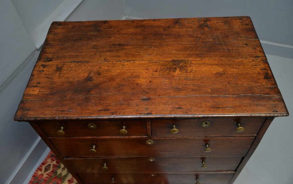 An early eighteenth-century Georgian oak chest of drawers featuring a two-over-three drawer configuration, brass escutcheons, turned knobs, and shaped bracket feet. View XV