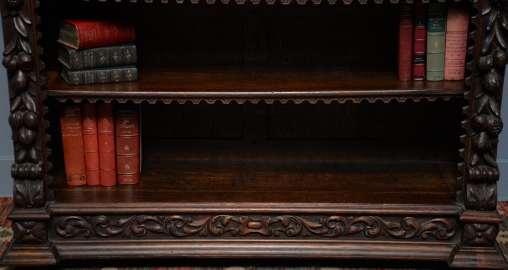 A low solid oak open bookcase decorated with hand-carved Green Man motifs, foliate pilasters, three shelves with scalloped edges, and a plinth base. View IV