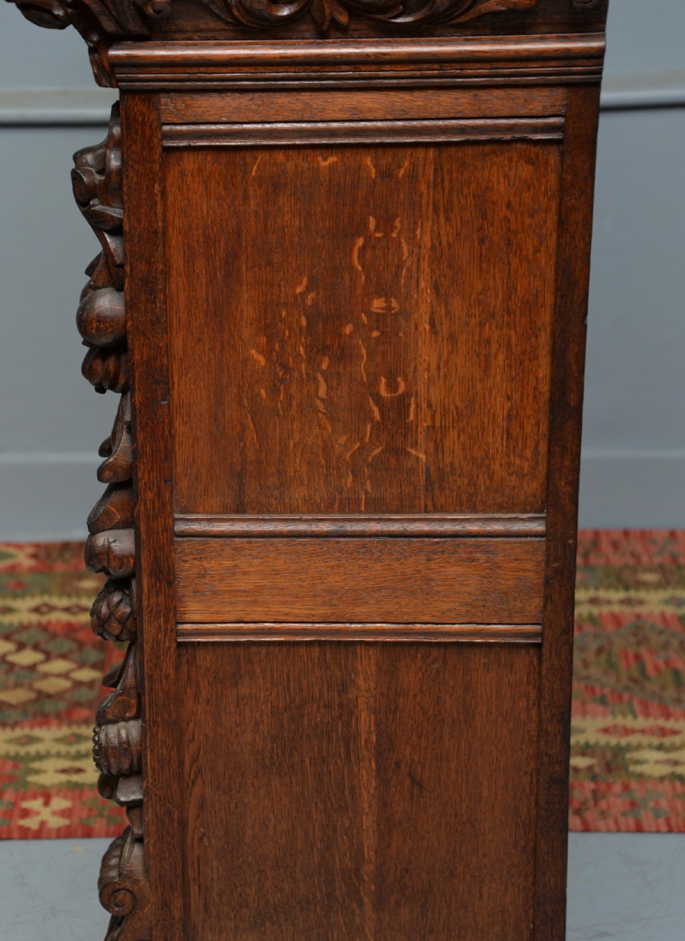 A low solid oak open bookcase decorated with hand-carved Green Man motifs, foliate pilasters, three shelves with scalloped edges, and a plinth base. View XXII