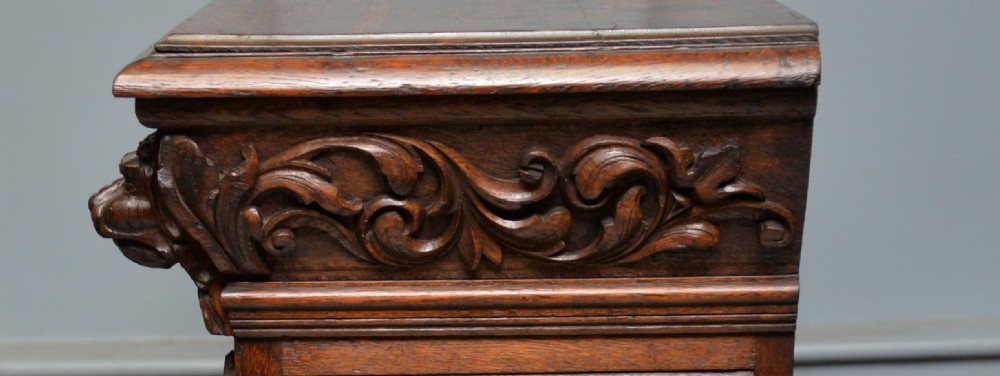 A low solid oak open bookcase decorated with hand-carved Green Man motifs, foliate pilasters, three shelves with scalloped edges, and a plinth base. View XXIII