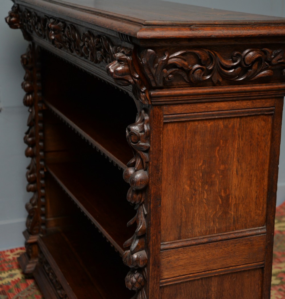 A low solid oak open bookcase decorated with hand-carved Green Man motifs, foliate pilasters, three shelves with scalloped edges, and a plinth base. View XXV