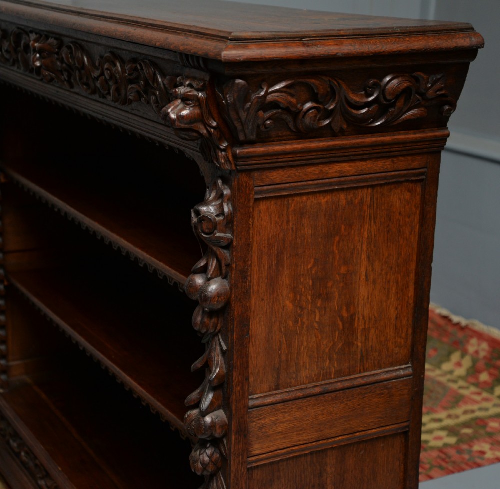 A low solid oak open bookcase decorated with hand-carved Green Man motifs, foliate pilasters, three shelves with scalloped edges, and a plinth base. View XXVI