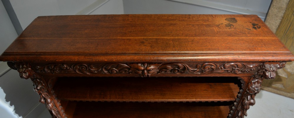 A low solid oak open bookcase decorated with hand-carved Green Man motifs, foliate pilasters, three shelves with scalloped edges, and a plinth base. View XXVIII