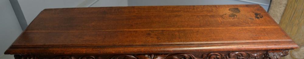 A low solid oak open bookcase decorated with hand-carved Green Man motifs, foliate pilasters, three shelves with scalloped edges, and a plinth base. View XXIX