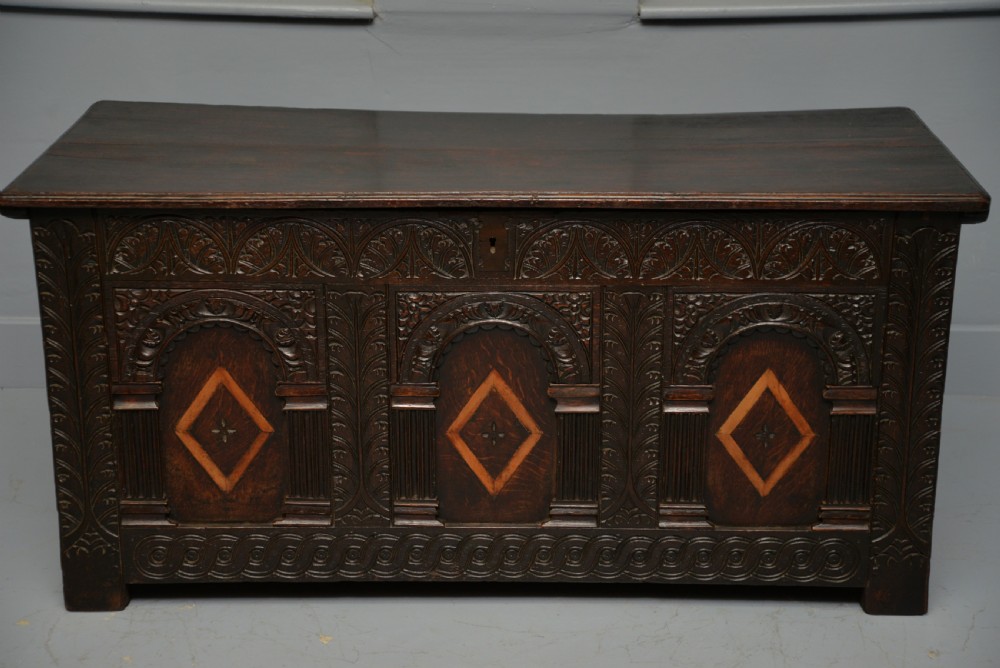 A 17th-century dark oak coffer featuring three carved arcaded front panels with diamond marquetry inlays and detailed frieze carving.