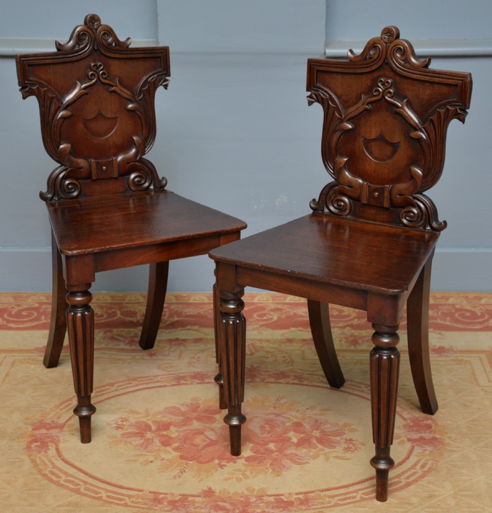 A pair of Regency mahogany hall chairs featuring carved scroll backs with shield motifs and turned reeded front legs.